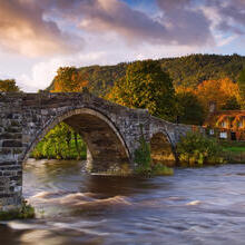 Large stone arched bridge over a flowing river. Sunset