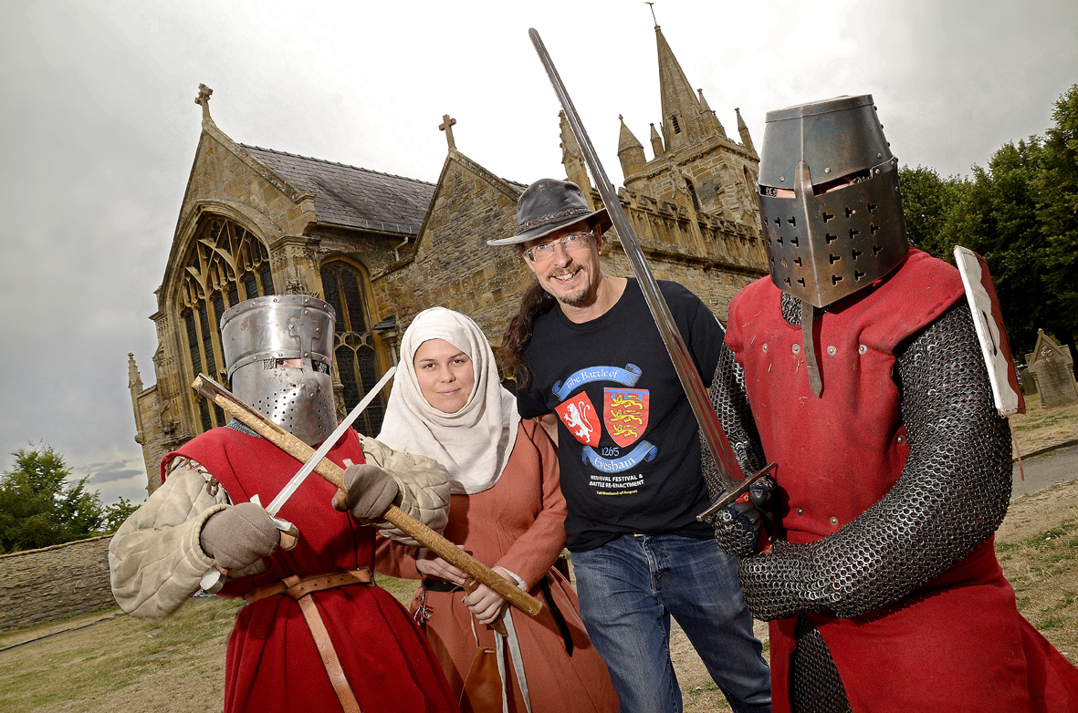 Four people in medieval costumes, including two in chainmail and helmets, pose with swords outside a historic church.