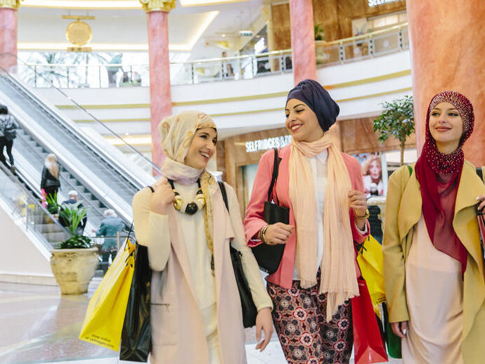 Tre donne con hijab che portano borse della spesa camminano in un centro commerciale di lusso.