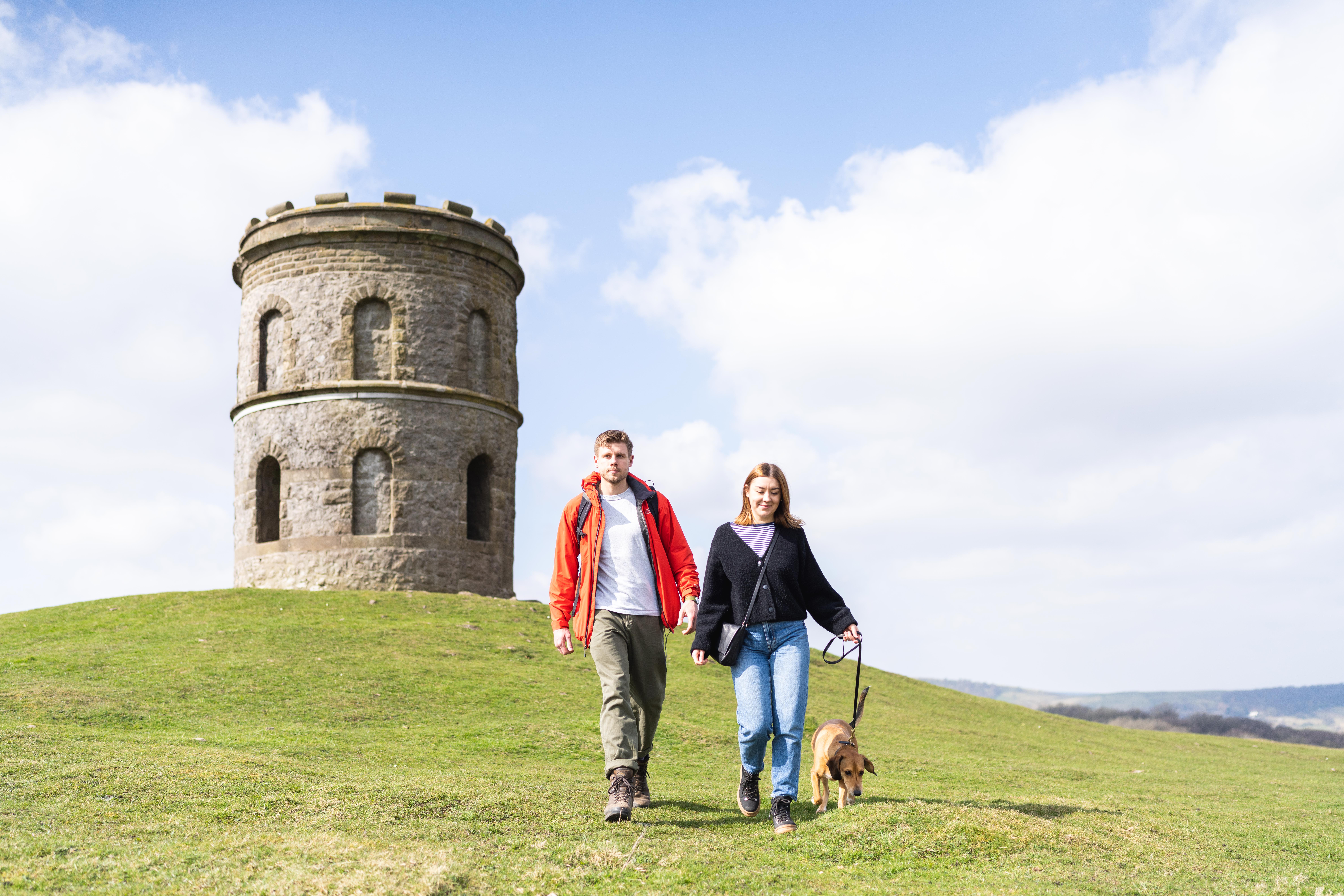 A young couple with a dog walking in Buxton Country Park with Solomon's Temple behind