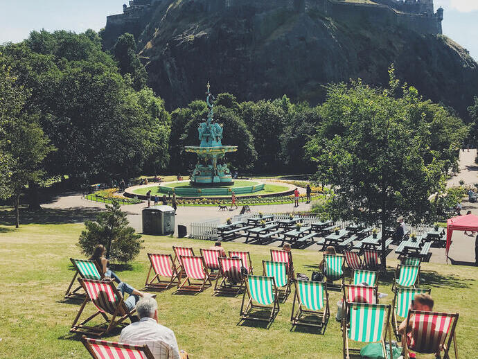 Grüne und rote Liegestühle auf dem Rasen in einem Park vor einem Schloss