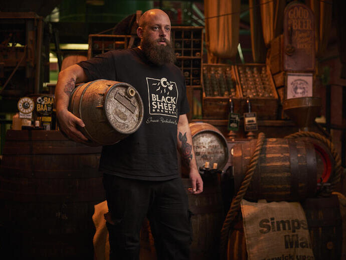 Mann, der in einem Lagerraum steht und ein Holzfass mit Bier hält