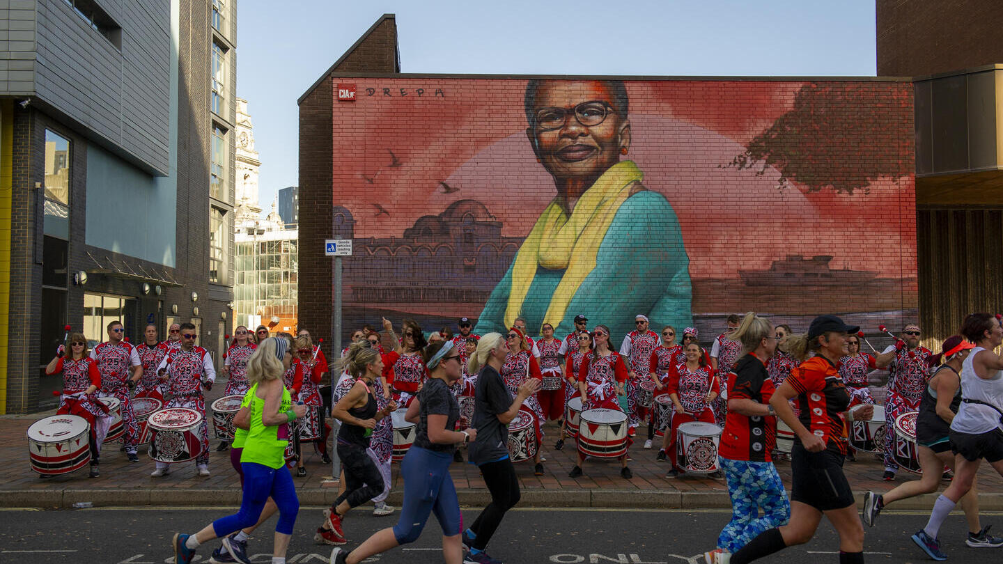 Persone che corrono davanti a una banda di percussionisti e colorate opere di street art