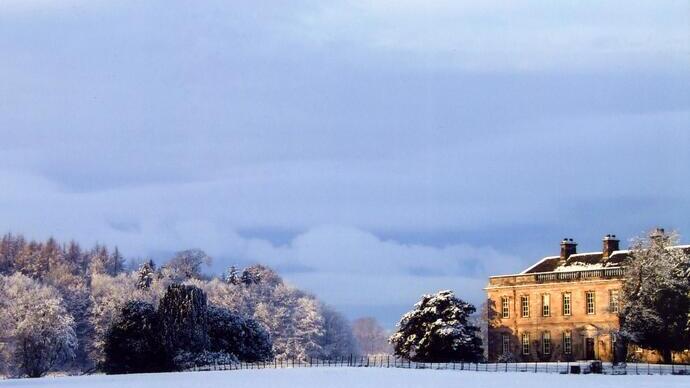 Large historic building on snowy landscape with trees and dramatic winter sky, evoking a peaceful and serene atmosphere.