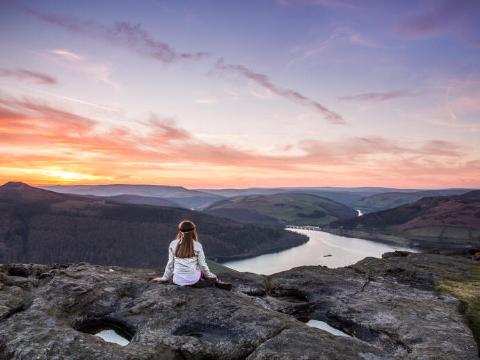 A woman sitting on rocks looking down valley to the river
