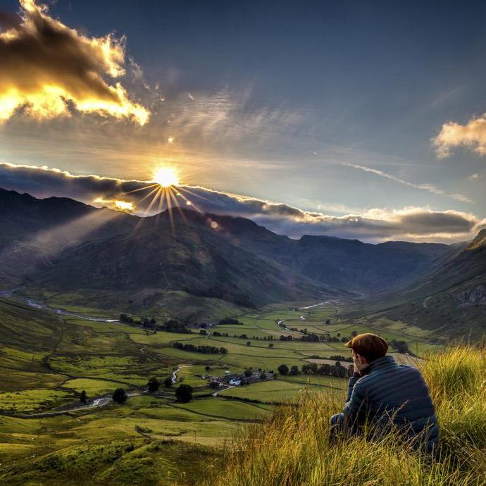 Mann, der im hohen Gras am Rande eines Hügels sitzt und den Sonnenuntergang beobachtet