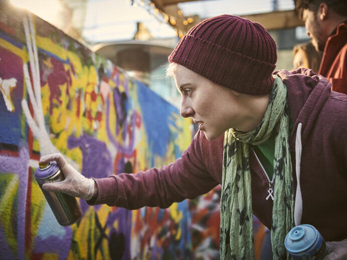Woman using a can of spray paint to create a street art mural