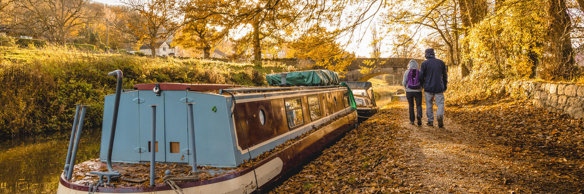 Two people walk alongside a canal in the autumn