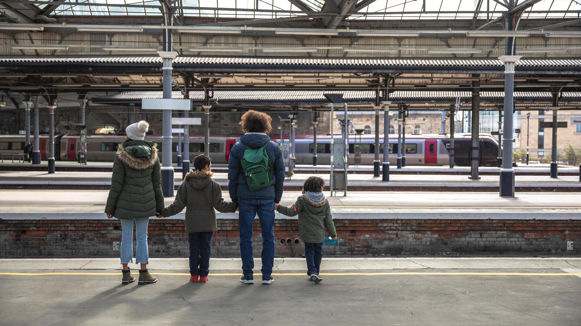 A multiracial family of four, a mother, father and their two little boys standing at Newcastle railway station platform waiting for their train.