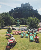 Green and red deck chairs laid out on grass in a park in front of a castle