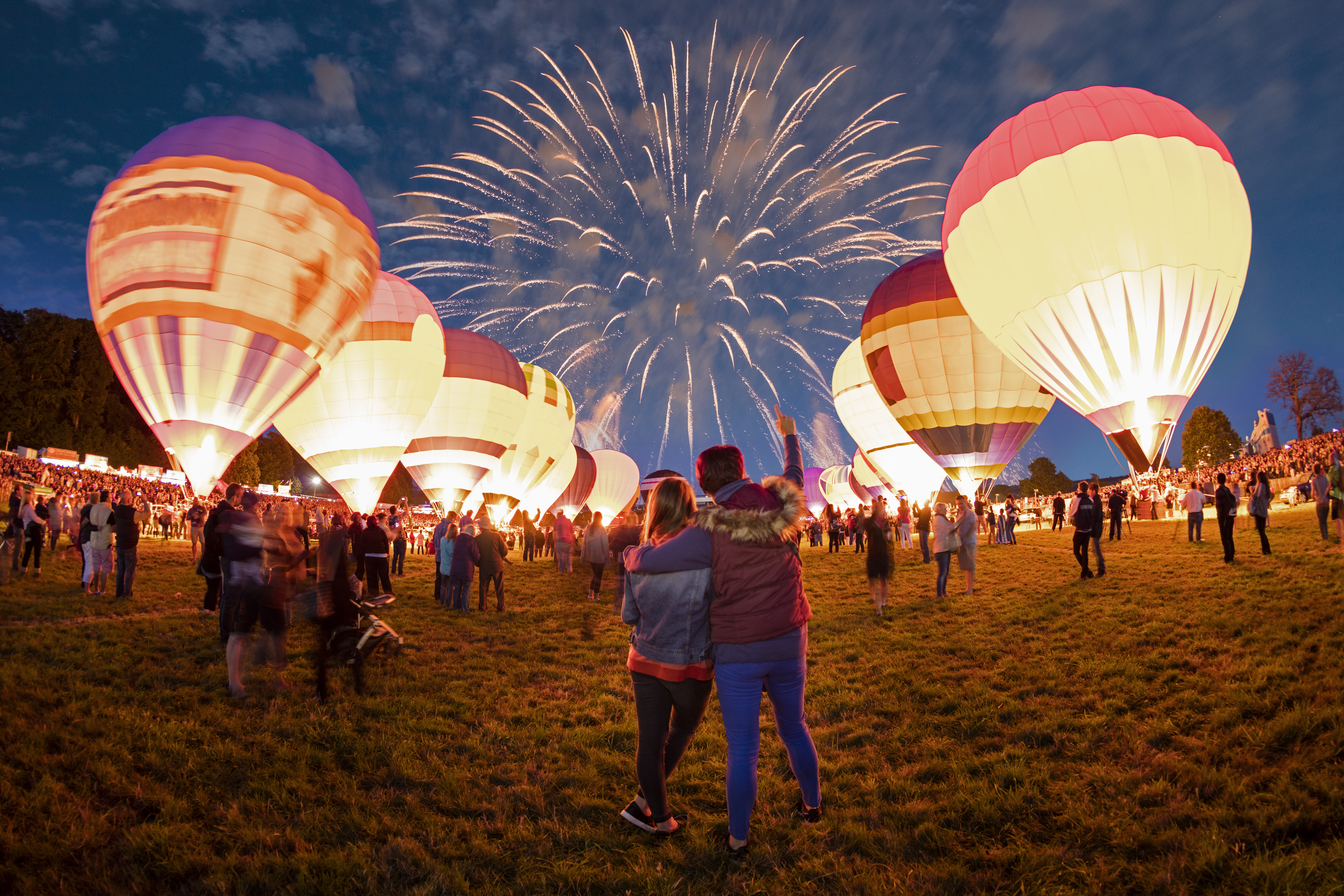 Couple watching grounded hot air balloons and fireworks in the night sky