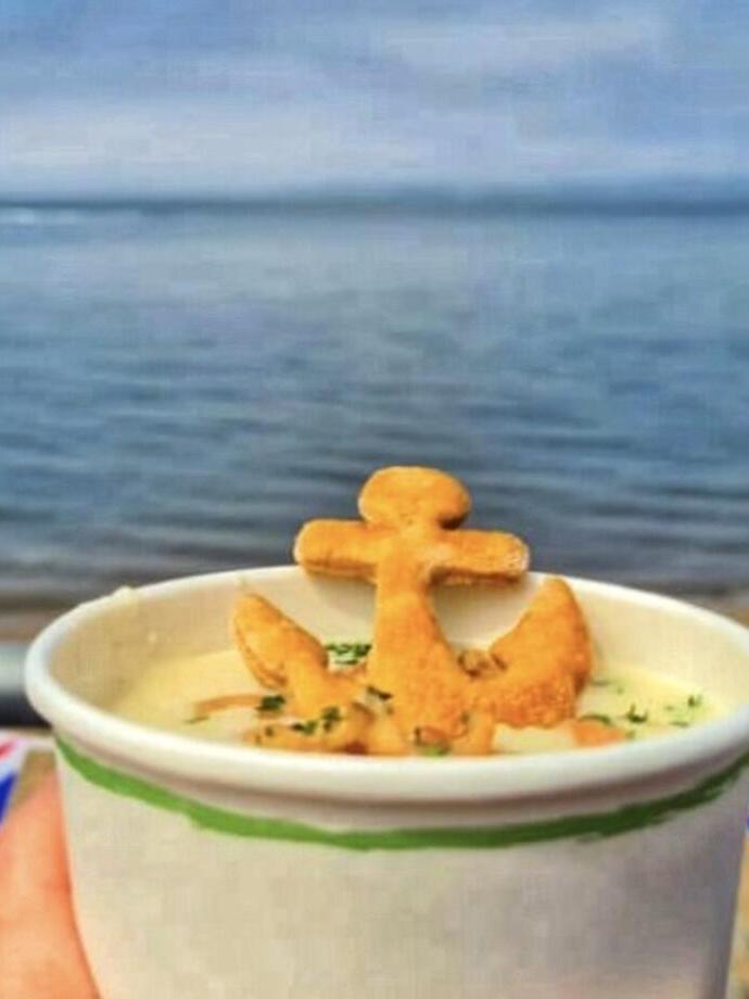 A pot of chowder with a pastry anchor looking across seafront 