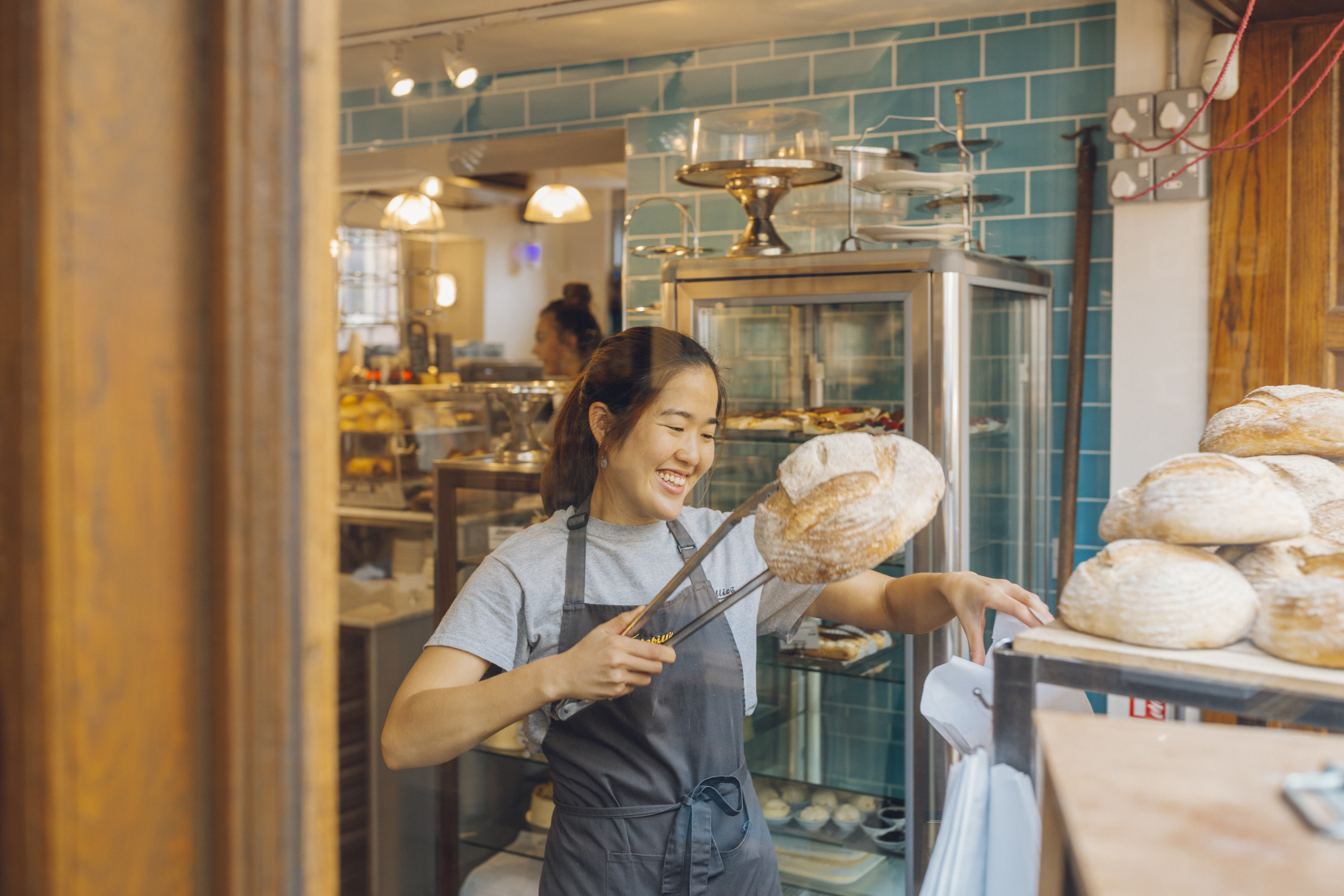 Smiling woman lifting loaf of bread with tongs