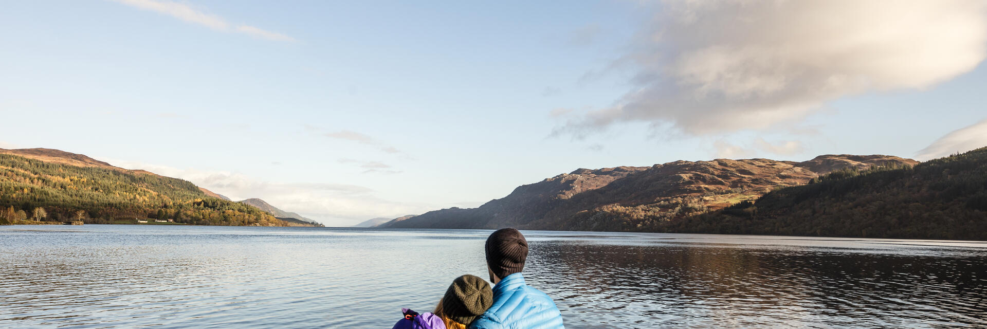 A man and woman sat looking across a lake