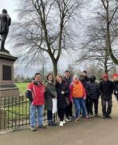 Un gruppo di turisti in visita guidata in posa vicino a una statua in un parco a Glasgow