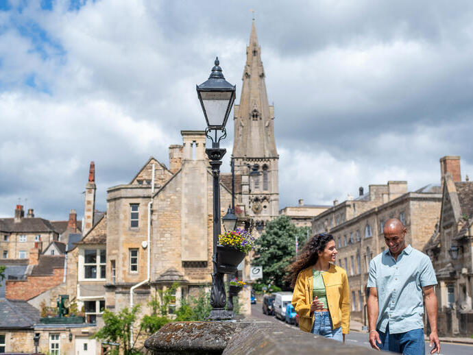 A man and a woman walk through a stone built village with a church