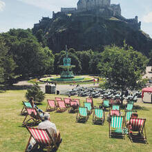 Green and red deck chairs laid out on grass in a park in front of a castle