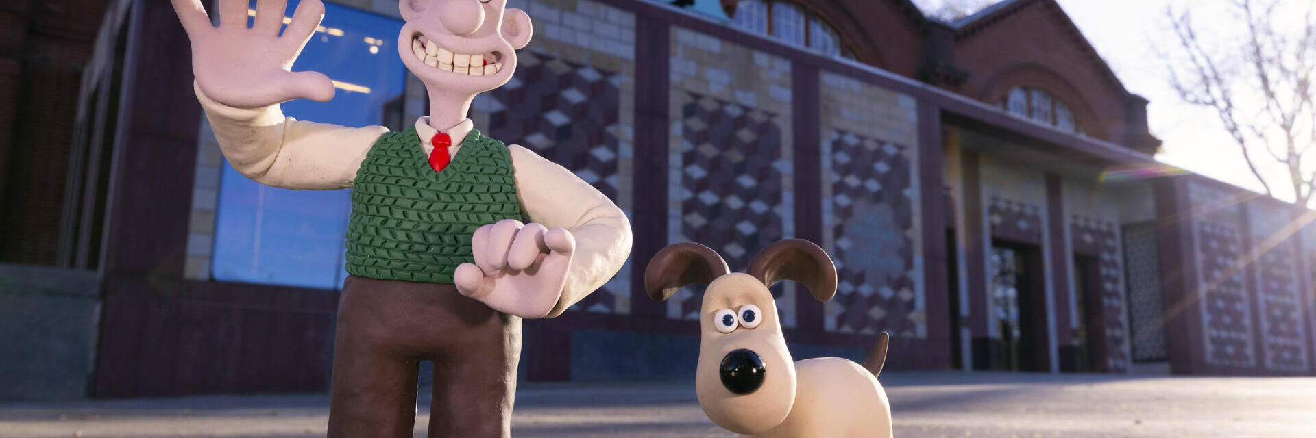 Clay animation characters stand outside a brick museum building with a large V&A sign, under clear sky.