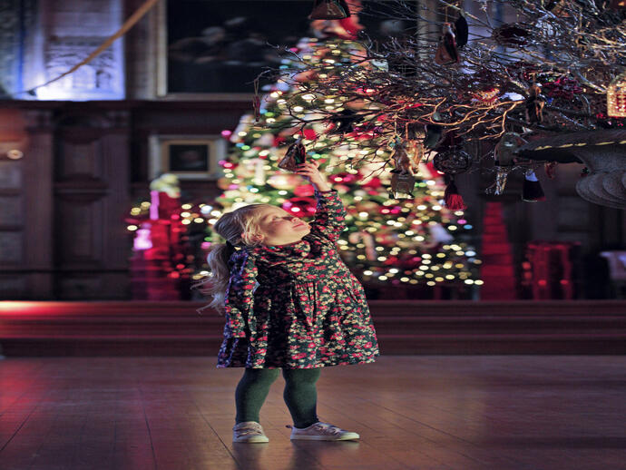 A girl looking at a hanging ornament in front of a decorated christmas tree at Bamburgh Castle's Christmas Kingdom