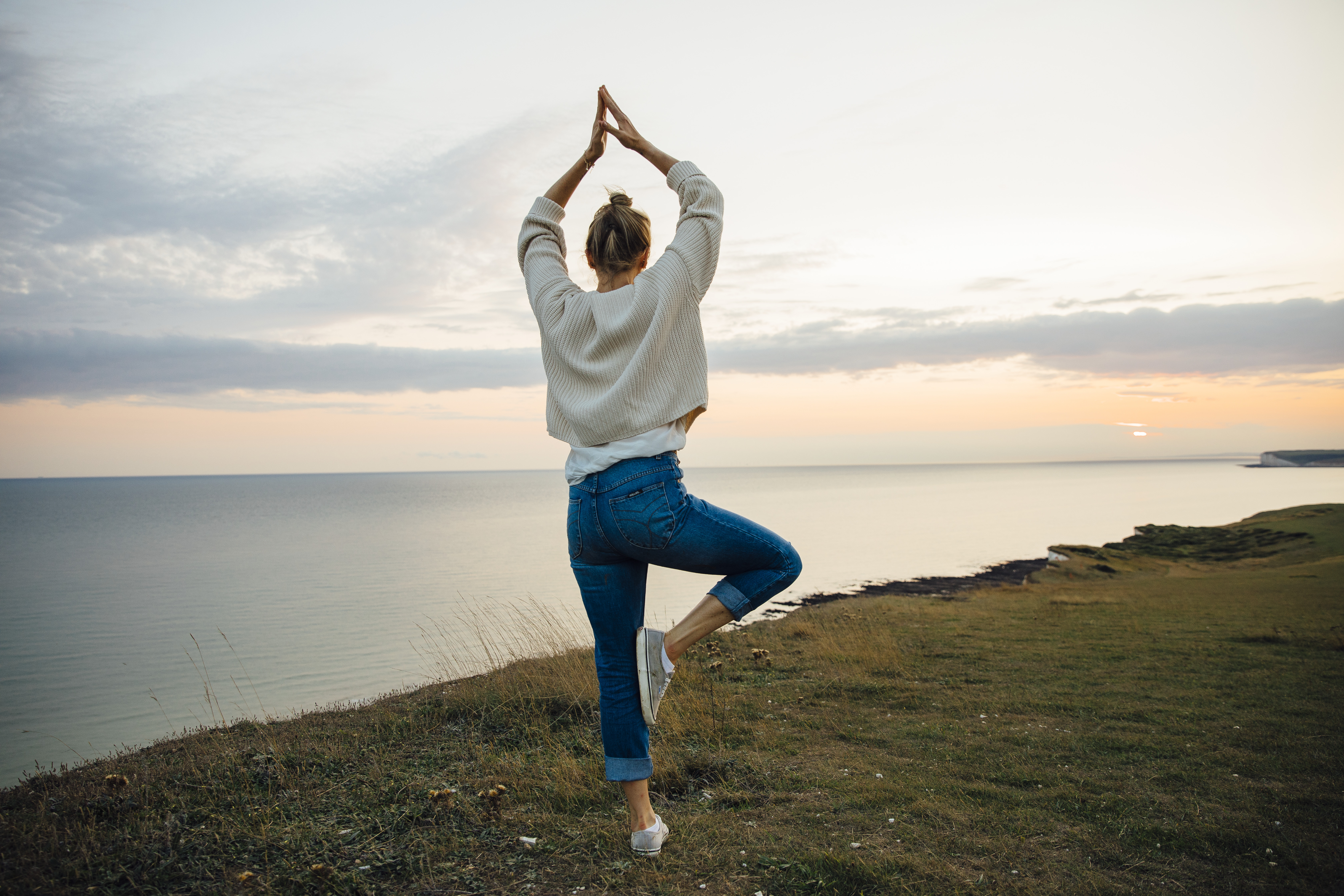 Mujer en una postura de yoga de pie en lo alto de un acantilado con vistas al mar