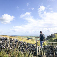 Man standing on stile over stone wall looking at landscape