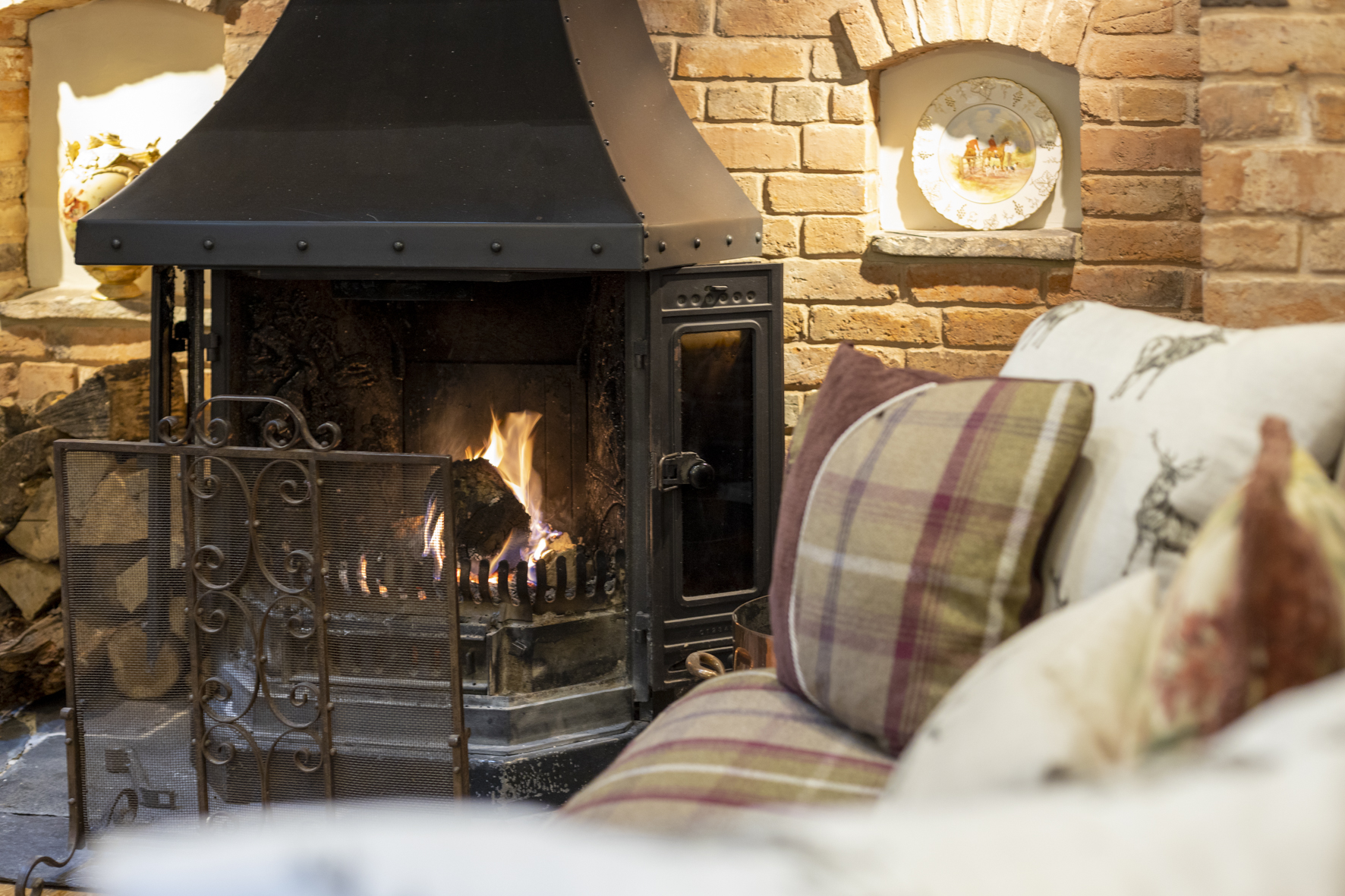 Close-up of the inglenook fireplace with fire and tartan patterned sofas.