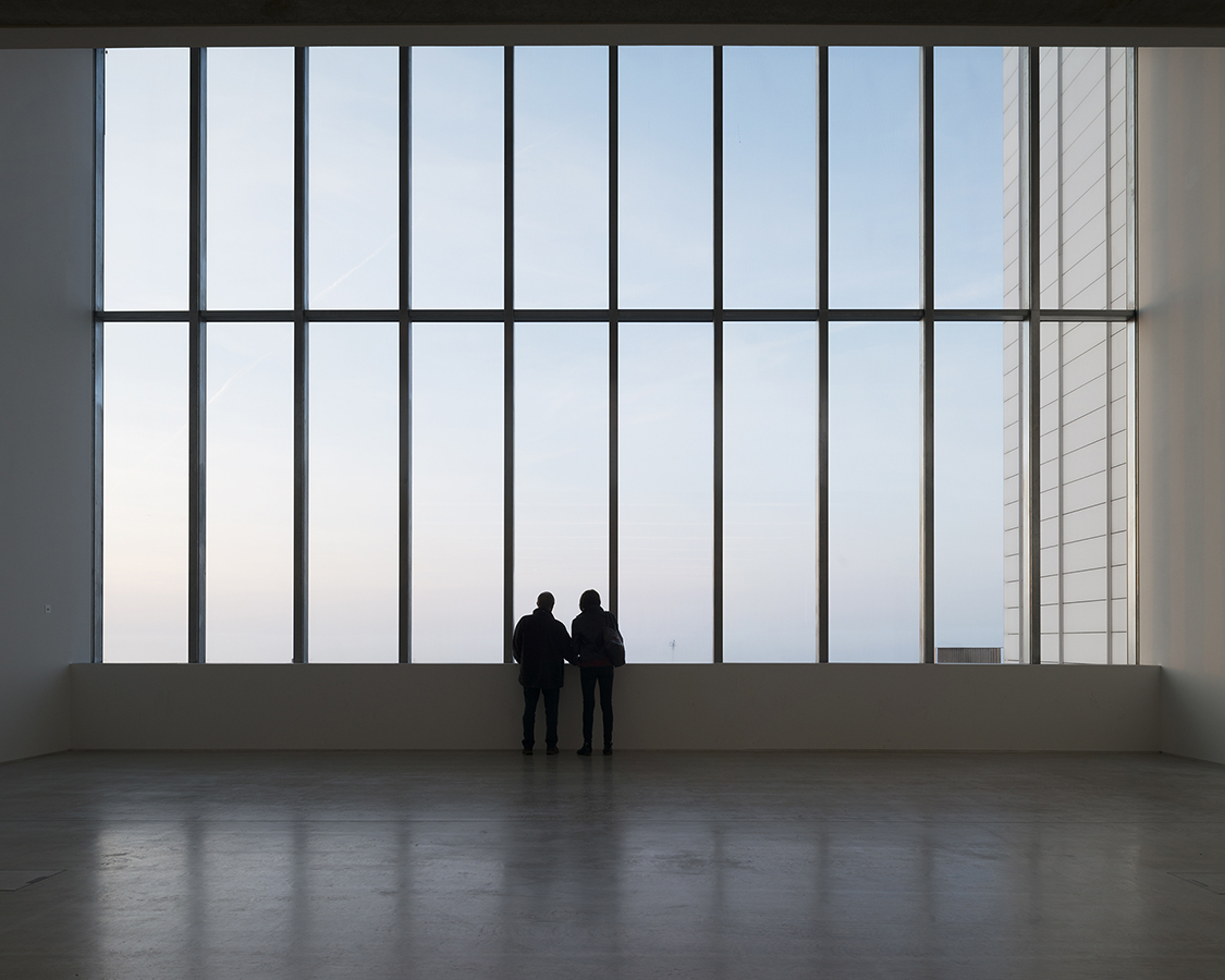 Two silhouetted people staring out of a wide window in a contemporary building