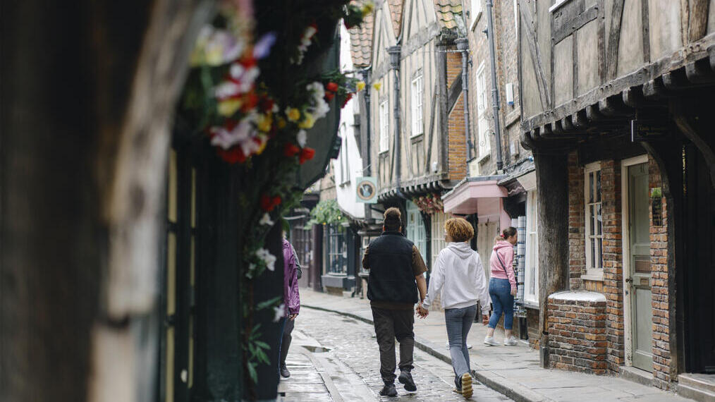 A man and a woman walk down a cobbled street holding hands
