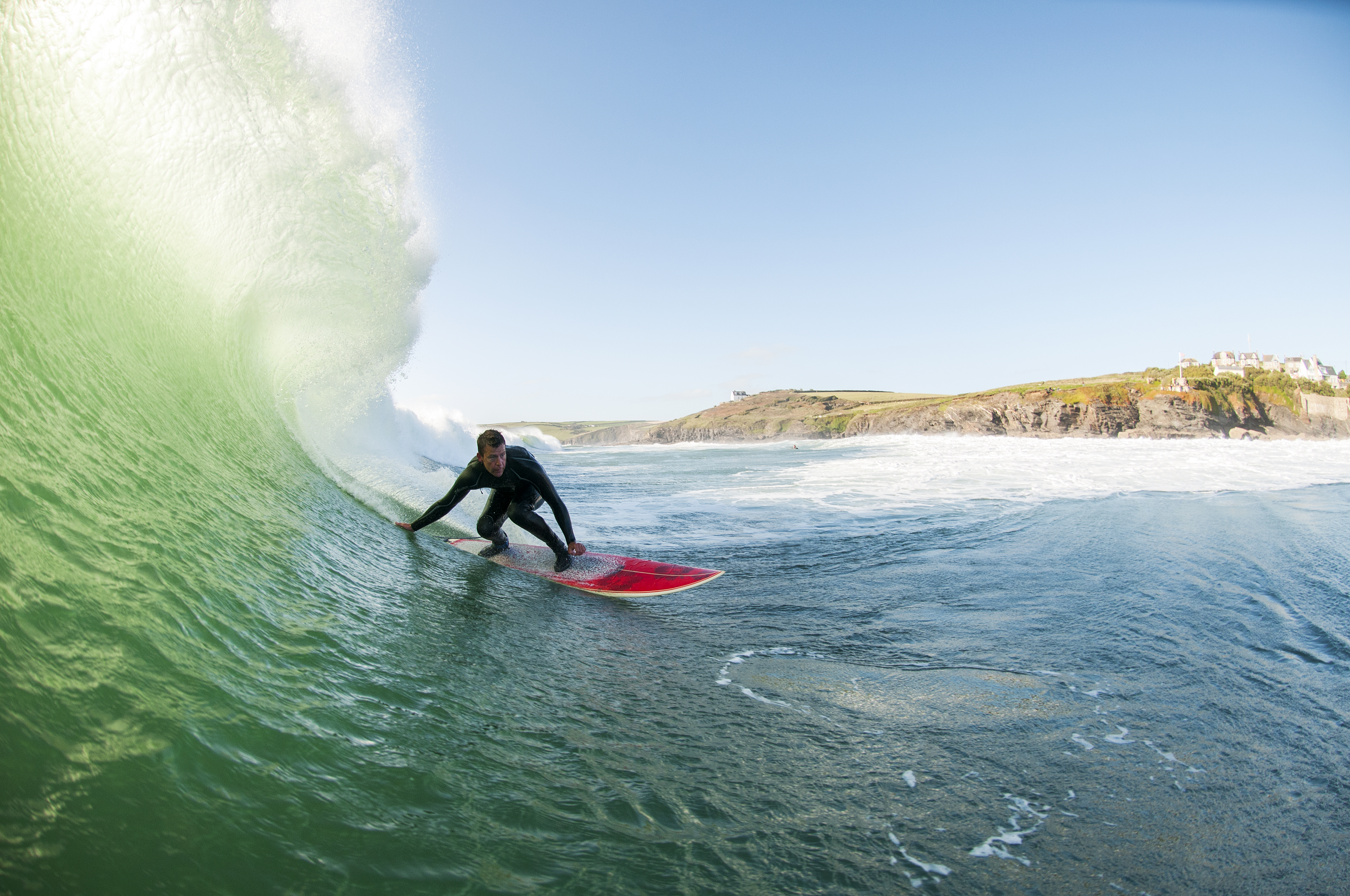 Surfer in a wetsuit surfing a large wave on a red surfboard in the sea