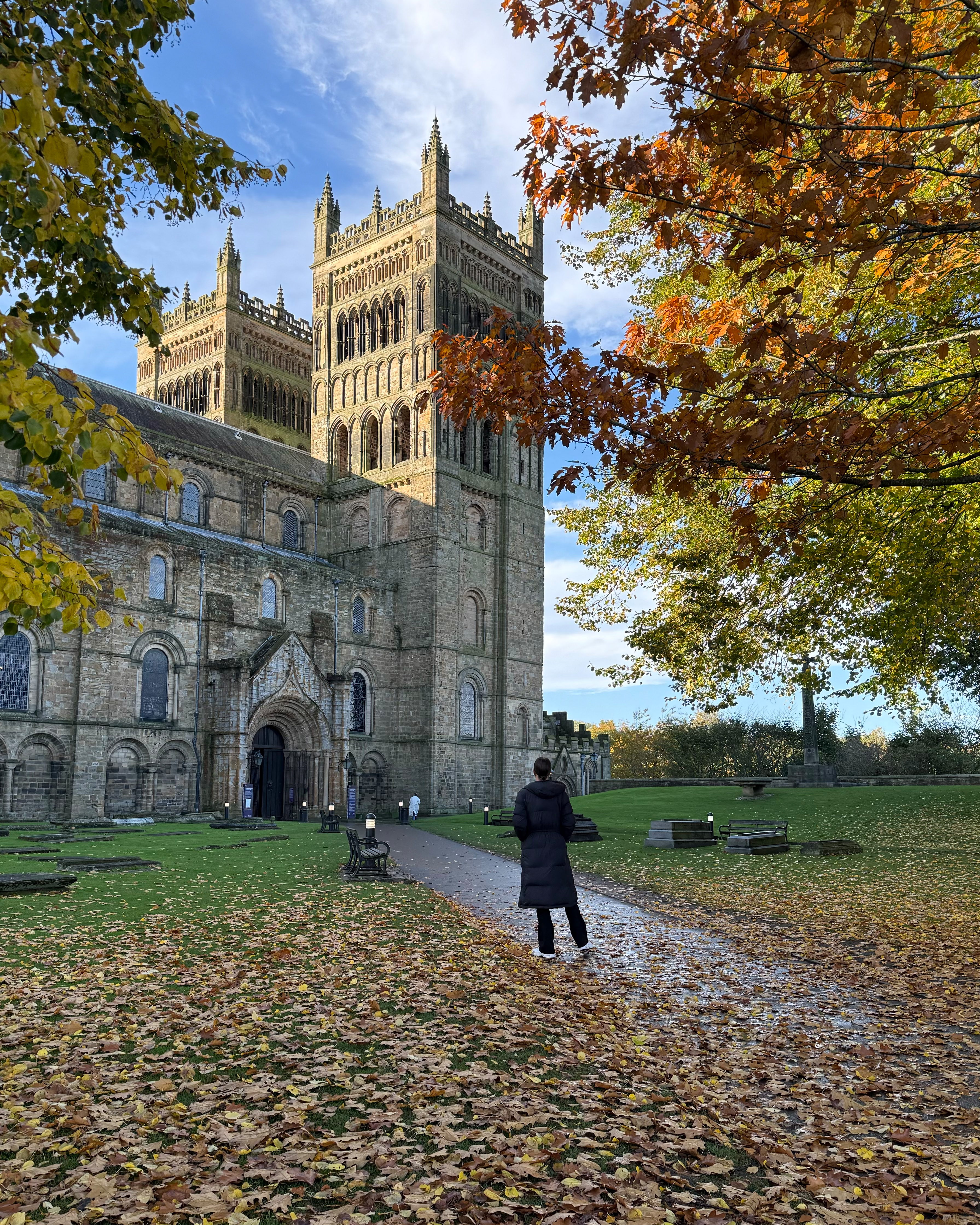 A woman in a warm jacket facing a large cathedral and tower.