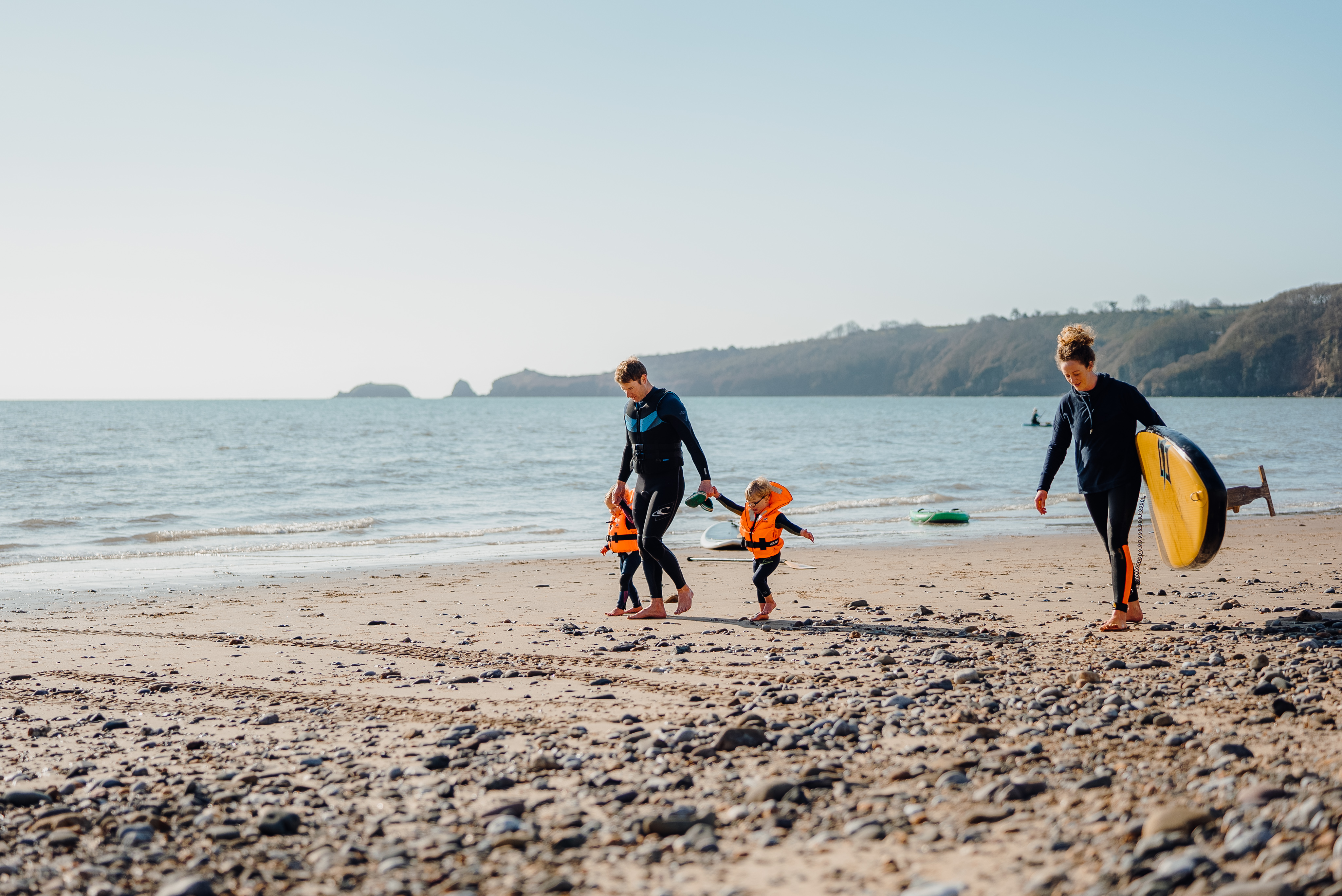 Una famiglia passeggia sulla spiaggia: l'uomo è con due bambini piccoli e la donna tiene in mano una tavola da surf a Saundersfoot Beach