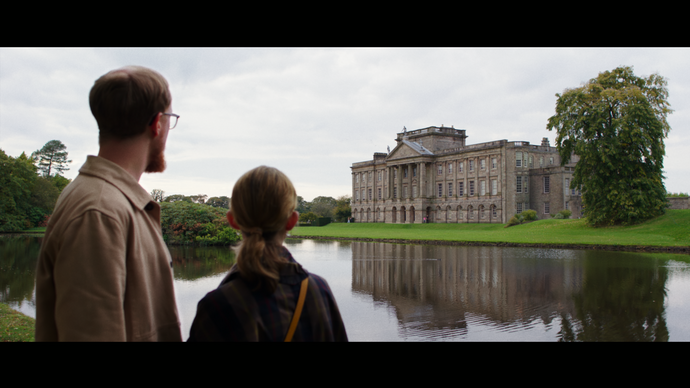 A man and a woman stand across a lake looking toward a heritage house