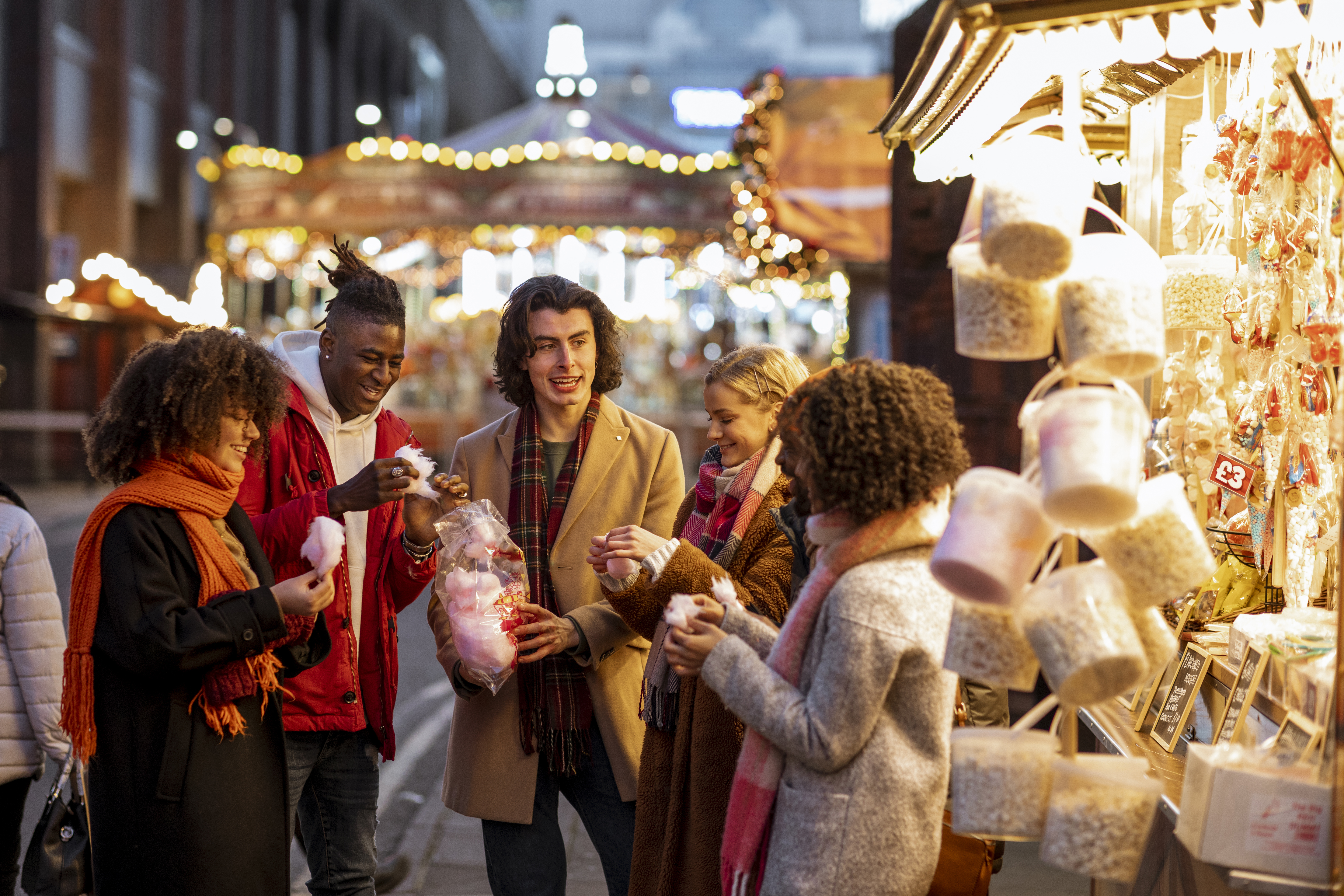Group of young friends sharing a bag of cotton candy at the Christmas market.