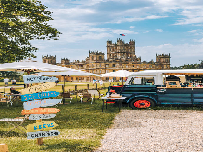 A food truck, parasols and direction signs in the ground of a castle