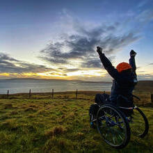 Wheelchair user, arms outstretched looking over the sea, watching the sunrise
