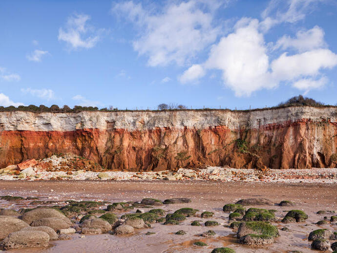 View of cliffs with white chalk overlaying red limestone in a colourful formation.