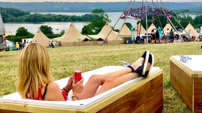 Woman sitting in a bath overlooking festival tents, with hills and a lake in the distance