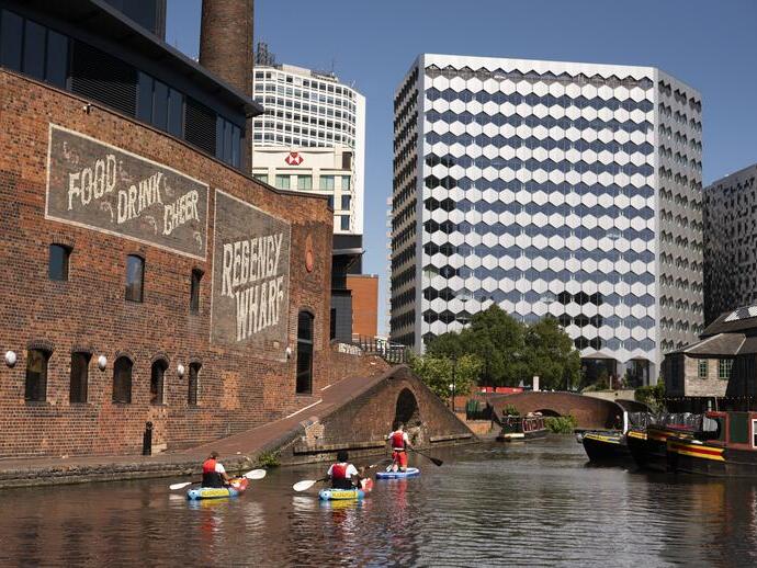 Group of people paddleboarding past industrial buildings on a canal