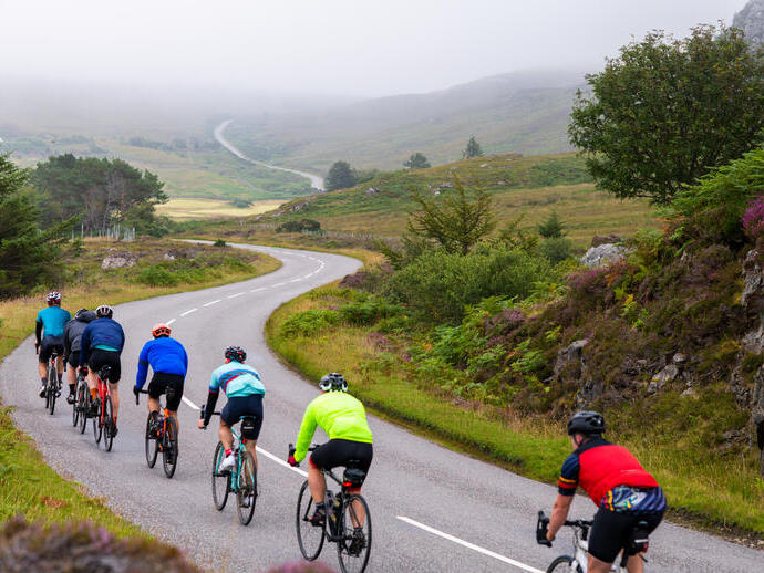 Professional cyclists riding on a twisty road through misty mountains