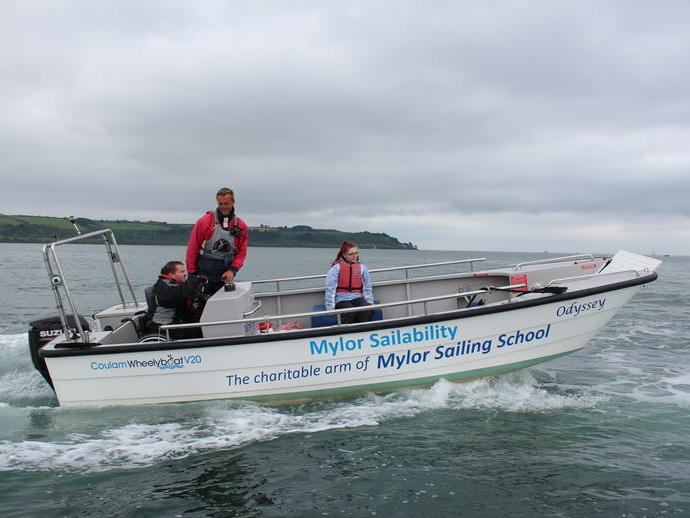 Uomo su una sedia a rotelle che guida una barca in mare accompagnato da un istruttore e da una donna
