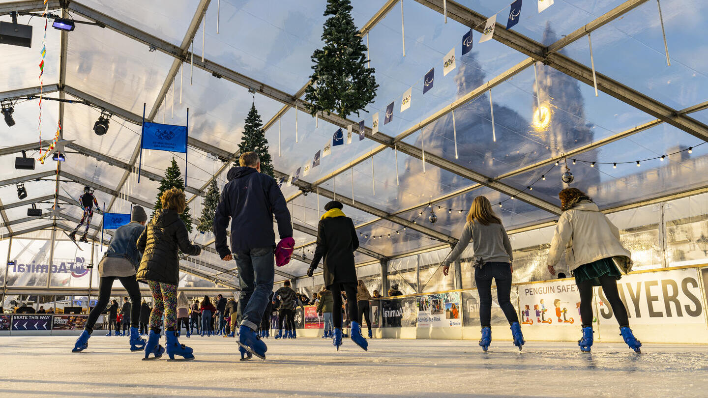 People ice skating on a skating rink under a glass ceiling