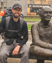 A man with walking sticks posing next to a statue on a bench in Glasgow