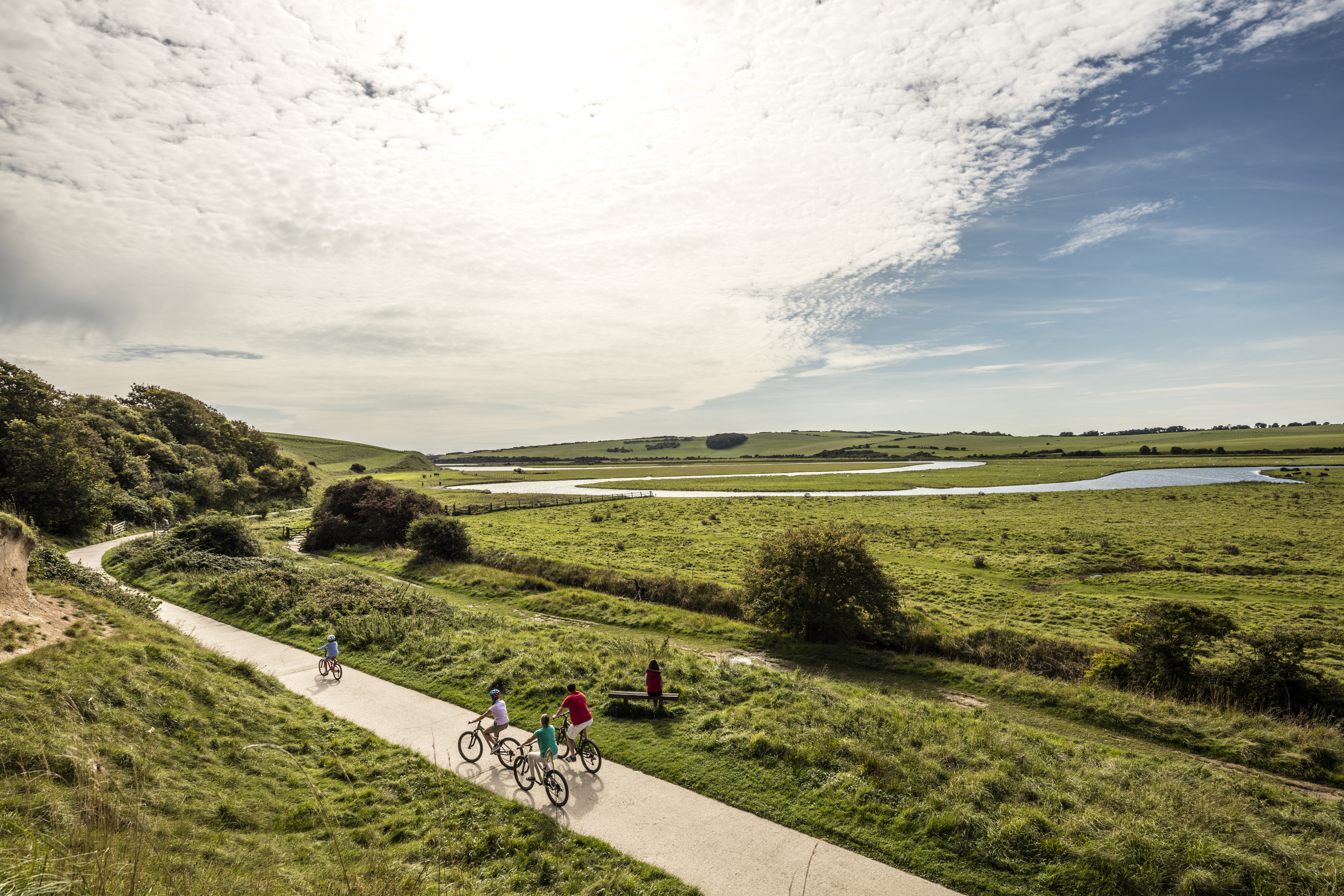 A family cycling along path through the wide open grassy English landscape.