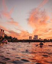 Atardecer sobre el río con personas en kayak cerca de edificios modernos.