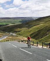 Cyclist riding on road through green dales