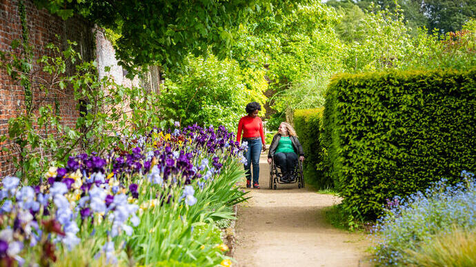Two women walking, one using a wheelchair, meandering through a garden path.