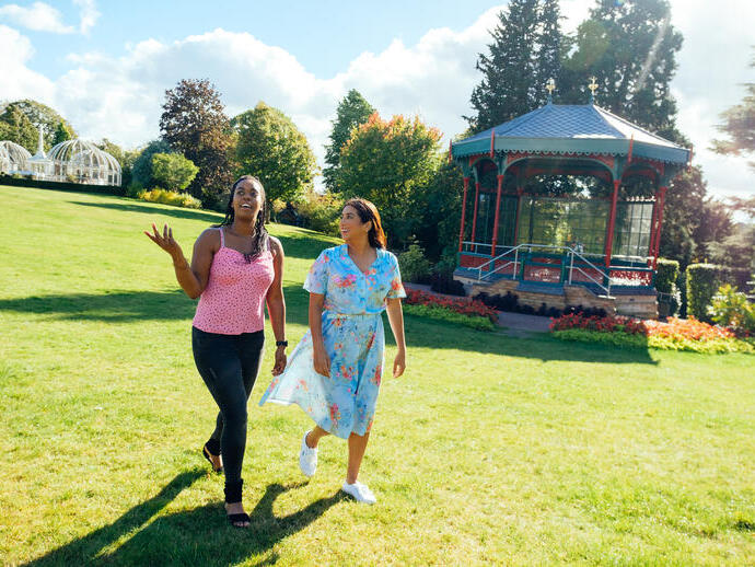 Two women walking on grass past a pergola