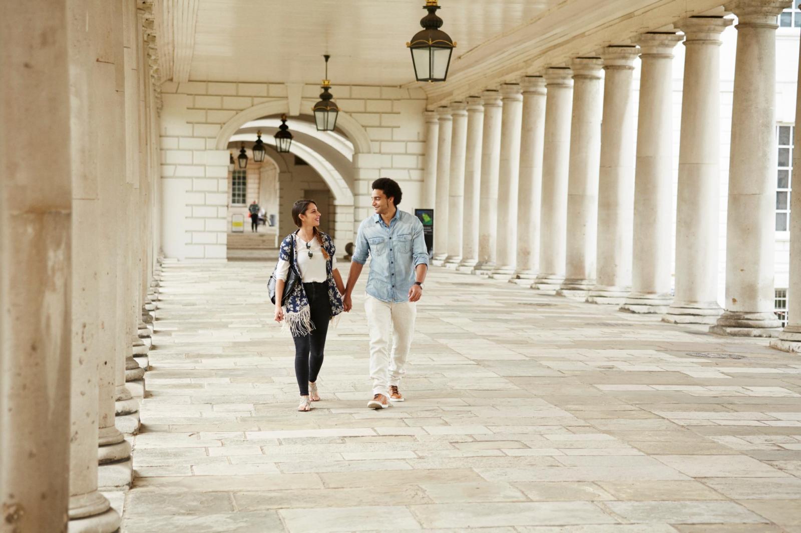 A hand in hand couple walking through marble colonnades.