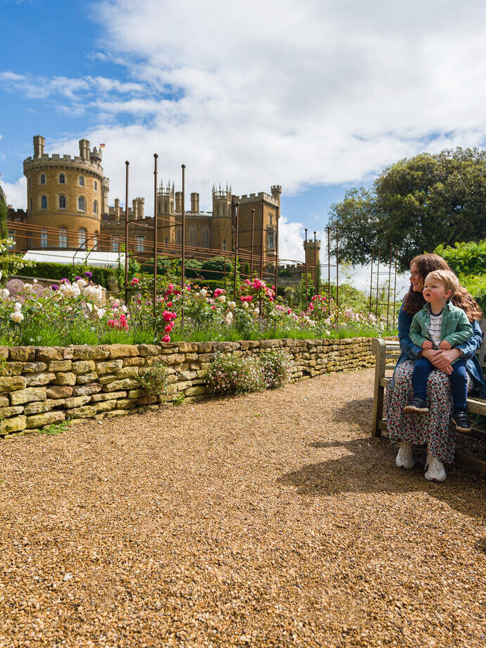 A woman sits on a bench with her child on her lap in front of a castle 