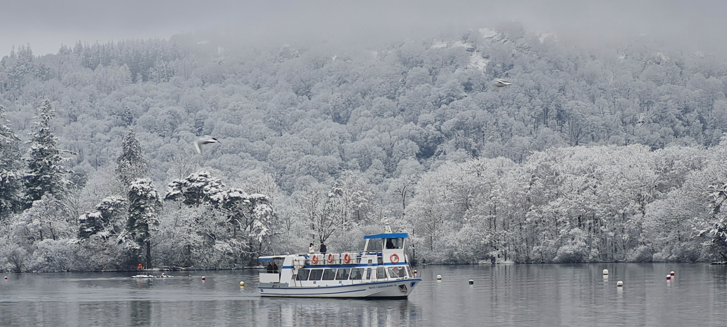 Boat on calm lake with snowy forested hills in the background, wintery and misty atmosphere.